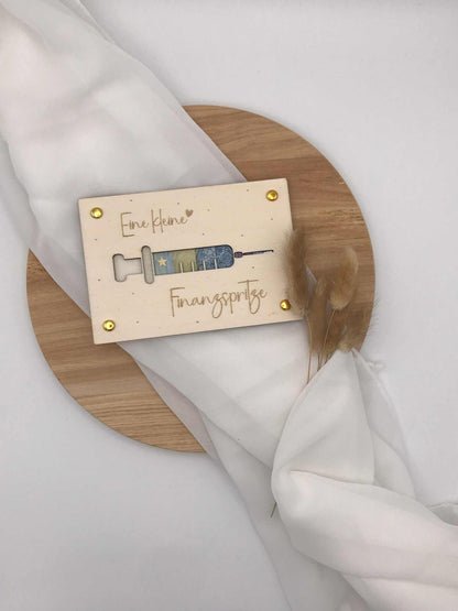 Kreativ verpackte Geldgeschenk-Karte "Finanzspritze" auf Holzplatte, dekorativ gestaltet.