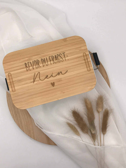 Brotdose mit Bambusdeckel, graviert, auf weißem Stoff mit dekorativem Gras.