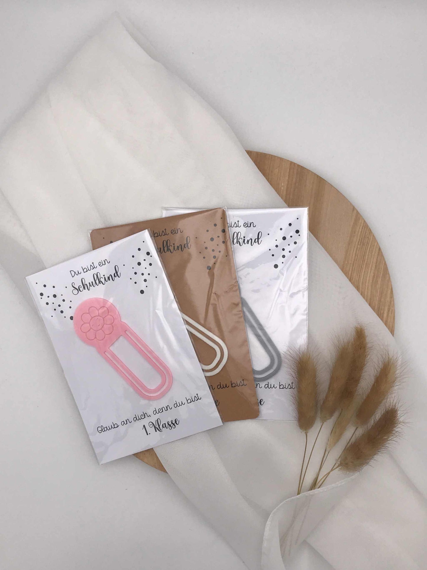 3D-gedruckte Lesezeichen für Schulanfänger in verschiedenen Farben auf Holzplatte, ideal als Geschenk zur Einschulung.