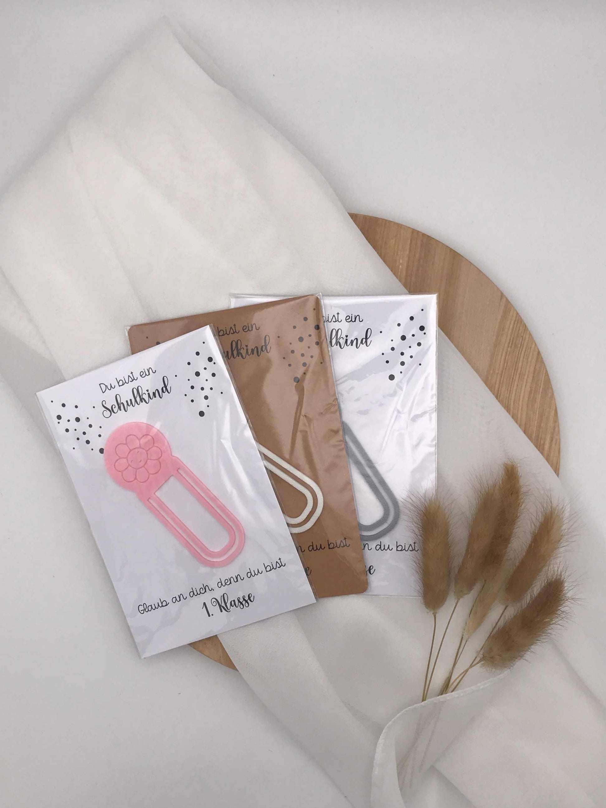 3D-gedruckte Lesezeichen für Schulanfänger in verschiedenen Farben auf Holzplatte, ideal als Geschenk zur Einschulung.