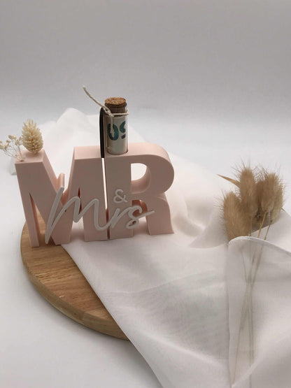 Geldgeschenk zur Hochzeit in 3D-Druck mit "Mr & Mrs" Schriftzug und Reagenzglas auf Holzunterlage.