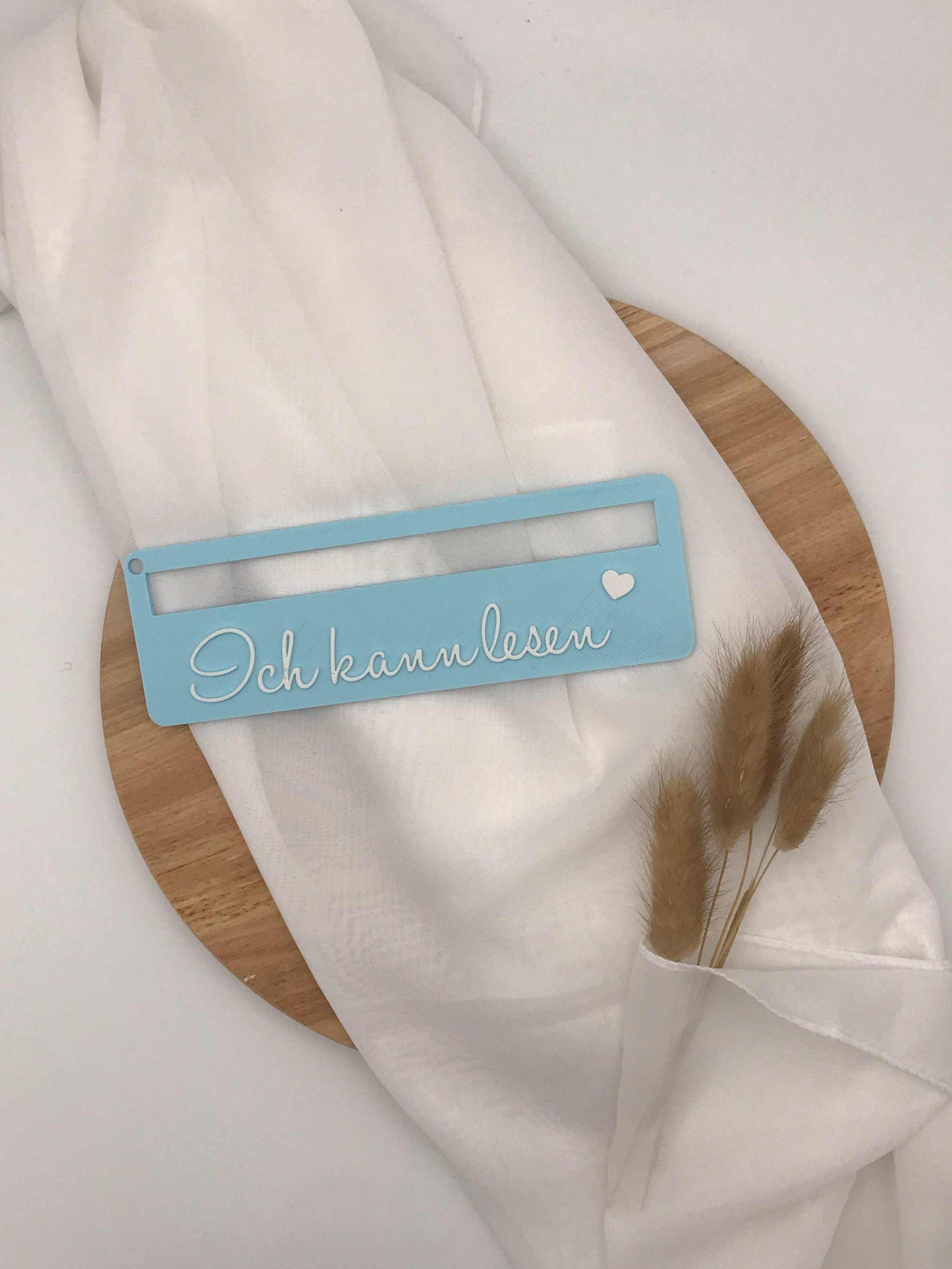Lesehilfe 3D-Druck für Schulanfänger in blau mit Aufschrift "Ich kann lesen", auf Holzplatte und Stoff drapiert.