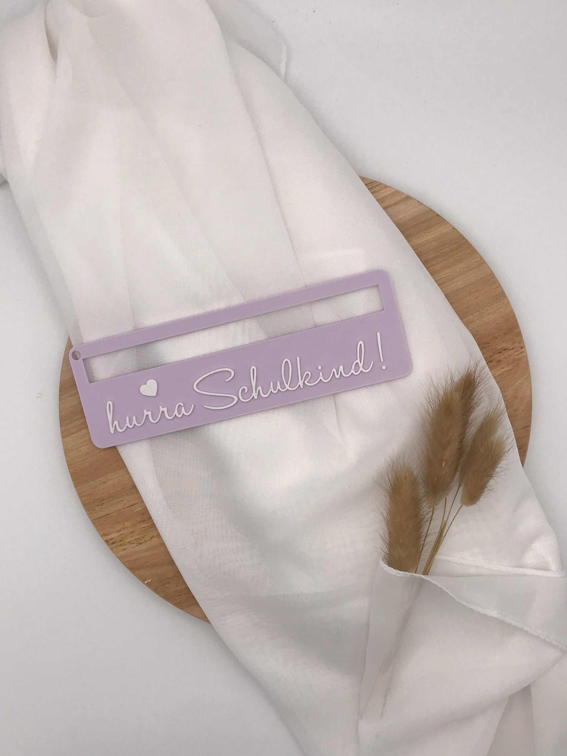 Lila 3D-gedruckte Lesehilfe mit Aufschrift "hurra Schulkind" für Schulanfänger auf weißem Stoff und Holzplatte