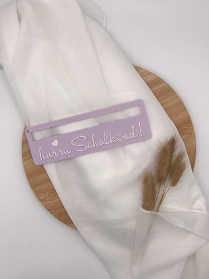 Lila 3D-gedruckte Lesehilfe mit Aufschrift "hurra Schulkind" für Schulanfänger auf weißem Stoff und Holzplatte