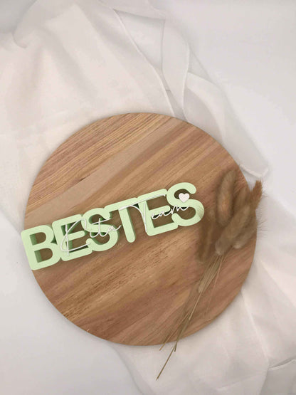 3D-Druck Aufsteller "Bestes Kita-Team" aus Holz auf weißem Stoff, dekorativ mit Trockenblumen arrangiert.