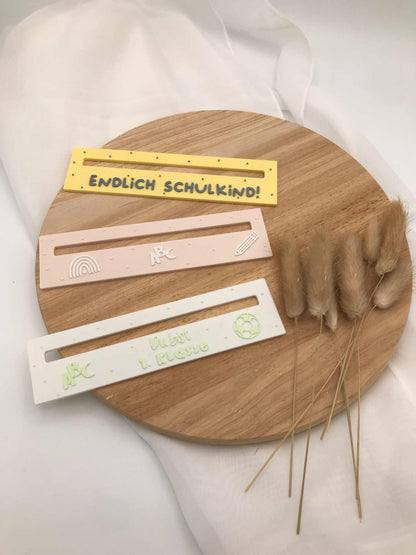 3D-gedruckte Lesehilfe für Schulanfänger, in bunten Farben und kindgerechten Motiven auf einem Holzteller dekoriert.
