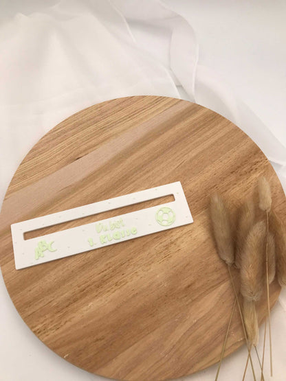 Lesehilfe aus 3D-Druck für Schulanfänger auf Holzplatte mit Trockenblumen.