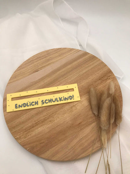 3D-gedruckte Lesehilfe für Schulanfänger in gelb mit der Aufschrift "Endlich Schulkind" auf einem Holzuntergrund.