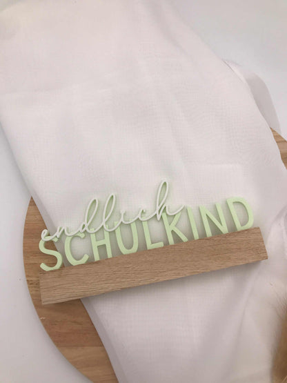 3D-gedruckter Schriftzug „Endlich Schulkind“ in hellem Grün als Einschulungsdekoration auf Holzständer