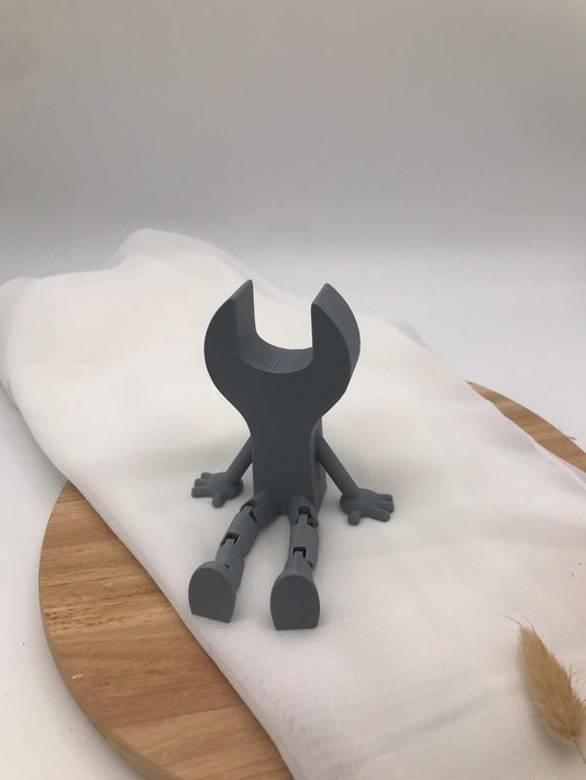 3D-printed gray decorative wrench figure with movable legs sitting on fabric and wooden surface
