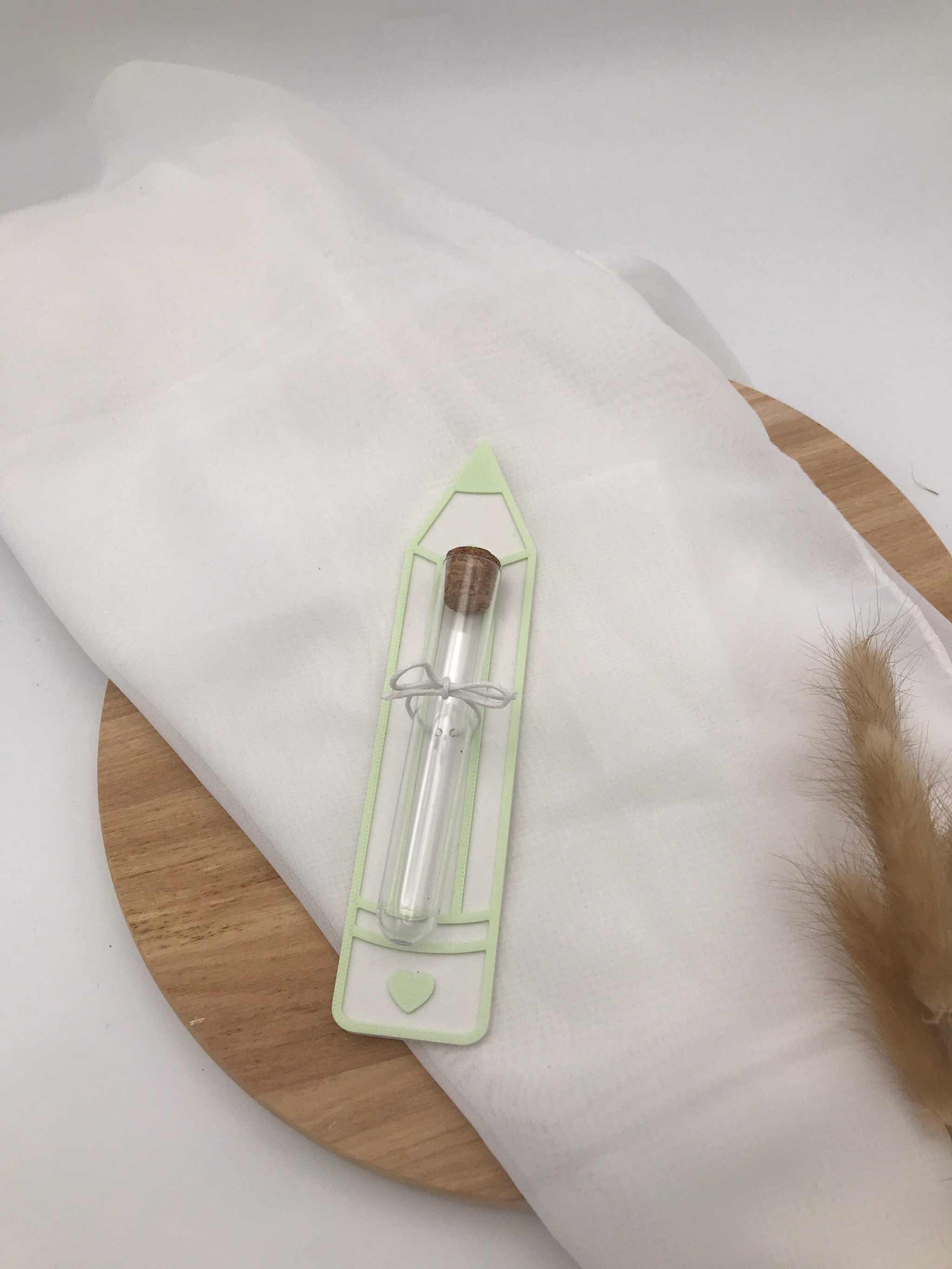 Geldgeschenk zur Einschulung in Stiftform aus 3D-Druck mit integriertem Reagenzglas und Korkverschluss, personalisierbar in grün, auf hellem Stoff und Holzplatte.