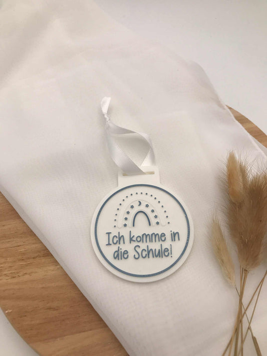 Round white 3D printed Medaille zur Einschulung with "Ich komme in die Schule!" text and rainbow design, gift for school enrollment.