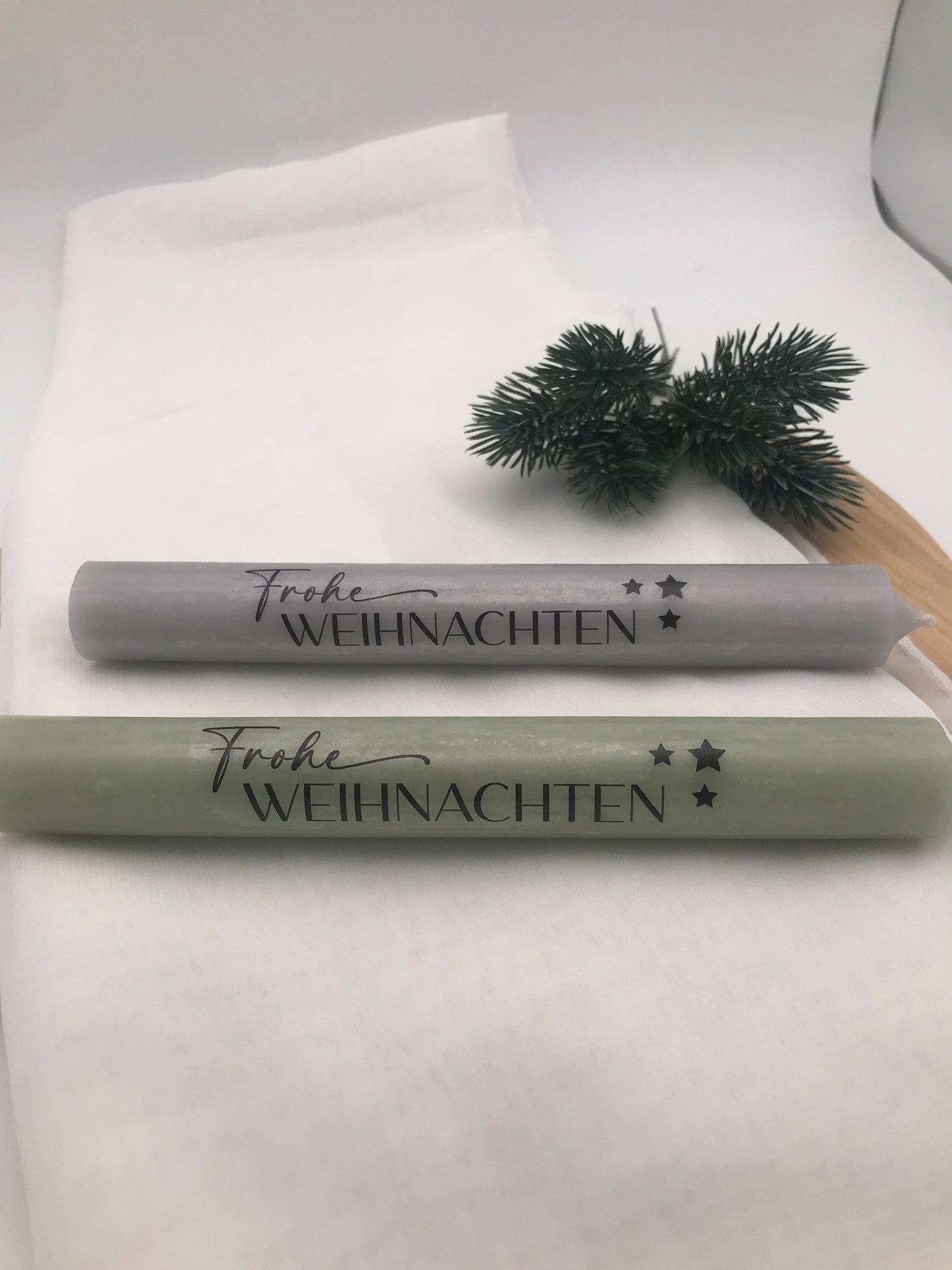 Festliche Stabkerzen in Grau und Grün mit Frohe Weihnachten Schriftzug und Tannenzweig als Weihnachtsdekoration