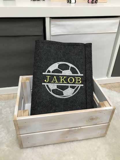 Grey felt certificate folder with a soccer design and personalized name, stored in a wooden box, perfect for organizing school documents.