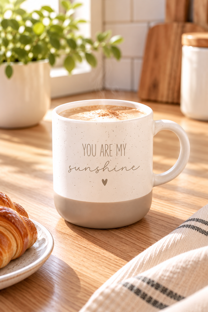 Kaffeetasse aus beiger Keramik mit grauem Fuß, feinem Sprenkelmuster und dem Schriftzug „You are my sunshine“