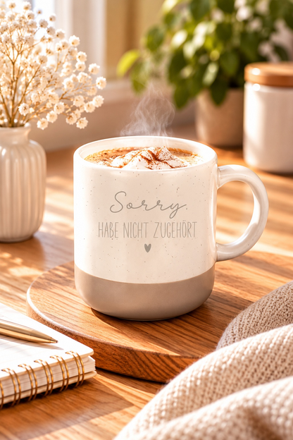 Kaffeetasse mit lustigem Spruch aus cremefarbener Keramik mit beigem Sockel und feinen Sprenkeln, bedruckt mit „Sorry, habe nicht zugehört“ und Herz