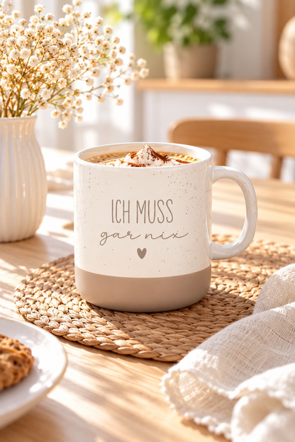 Kaffeetasse mit lustigem Spruch aus cremefarbener Keramik mit beigem Fuß und Schriftzug „Ich muss gar nix“