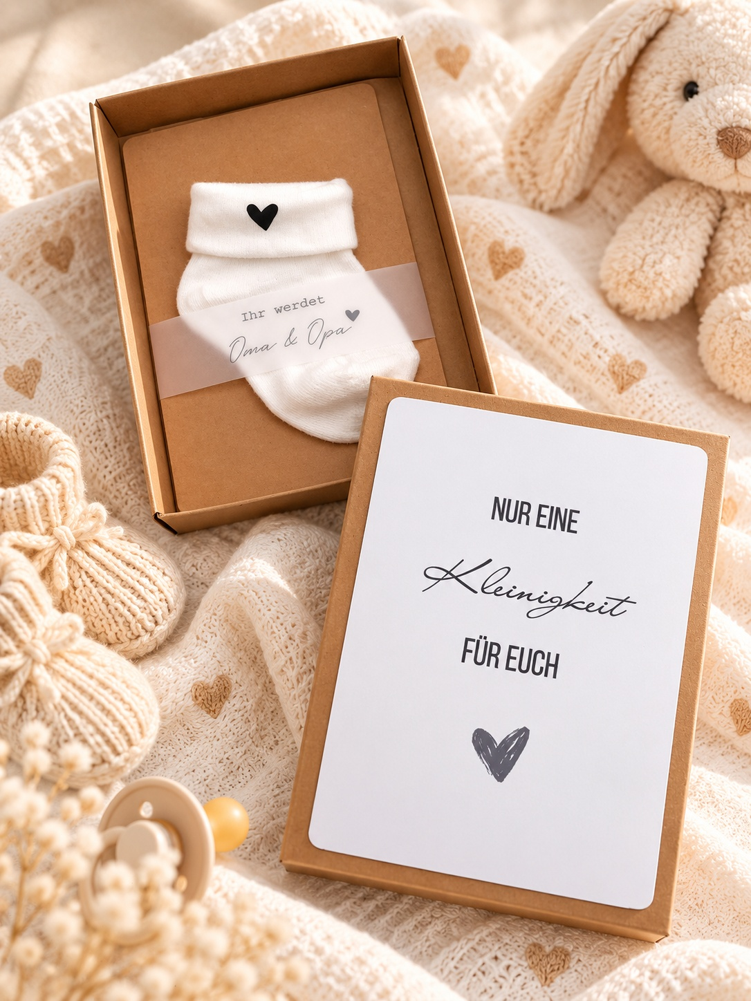 Schwangerschaft Geschenkbox aus braunem Kraftpapier mit weißer Babysocke und schwarzem Herz sowie herzlicher Botschaftskarte