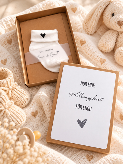 Schwangerschaft Geschenkbox aus braunem Kraftpapier mit weißer Babysocke und schwarzem Herz sowie herzlicher Botschaftskarte