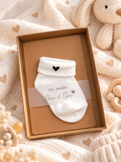 Schwangerschaftsankündigung als Geschenkbox aus braunem Kraftpapier mit weißer Babysocke und schwarzem Herz
