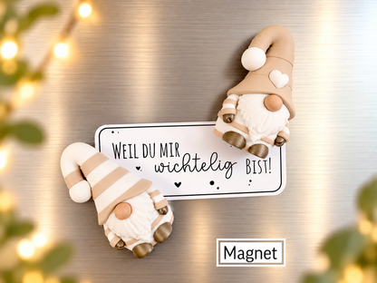 Wichtel Magnet aus beigefarbenem Kunststoff mit weißen Bärten, Zipfelmützen und Herz, neben einem Schild mit liebevollem Spruch